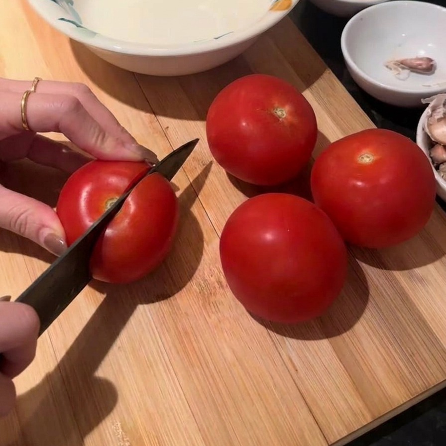 Des mains utilisant un couteau de chef pour couper une tomate rouge fraîche sur une planche en bois.