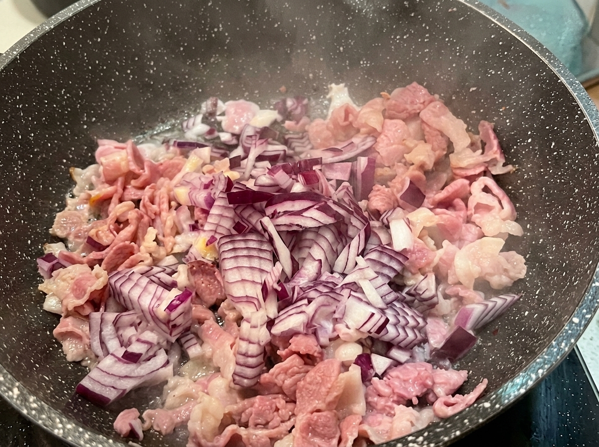 Dés doignon rouge parsemés sur des morceaux de bacon partiellement cuits dans une poêle chaude.