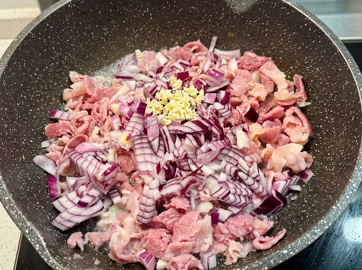 Un petit tas dail frais haché sur les oignons rouges et le bacon sautés dans une poêle.