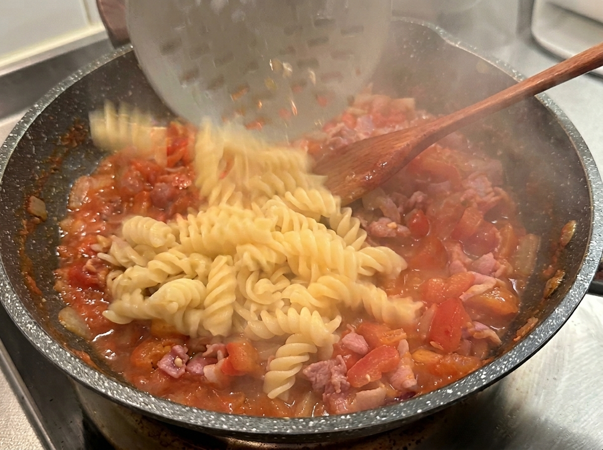 Fusilli cuits versés dune écumoire dans une poêle chaude de sauce tomate et bacon rouge.