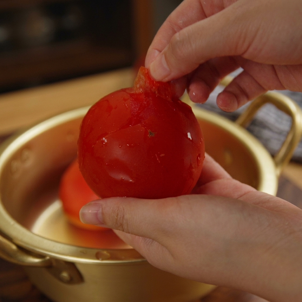 Mains retirant la peau dune tomate rouge éclatante au-dessus dun bol.