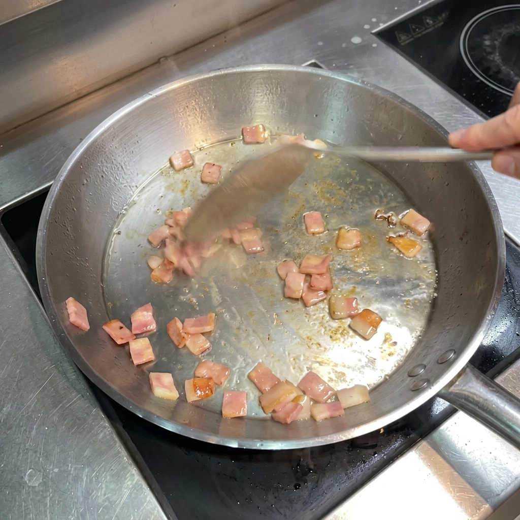 Une spatule en métal remuant des lardons bien dorés et croustillants dans la poêle.