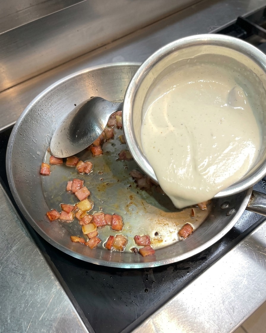 Crème liquide versée dun petit bol dans une poêle contenant le bacon croustillant.