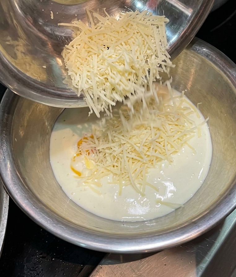 Fromage râpé tombant dun bol en métal dans le mélange crème et jaune dœuf.