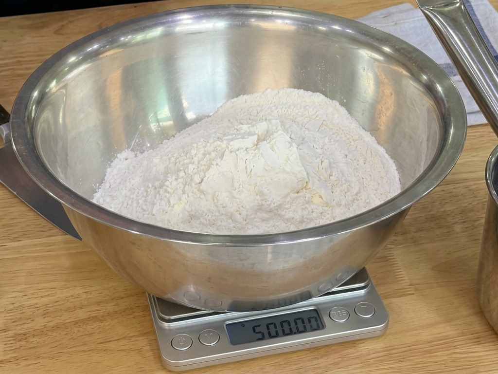 Un grand bol mélangeur en inox sur une balance numérique contenant une montagne de farine blanche.