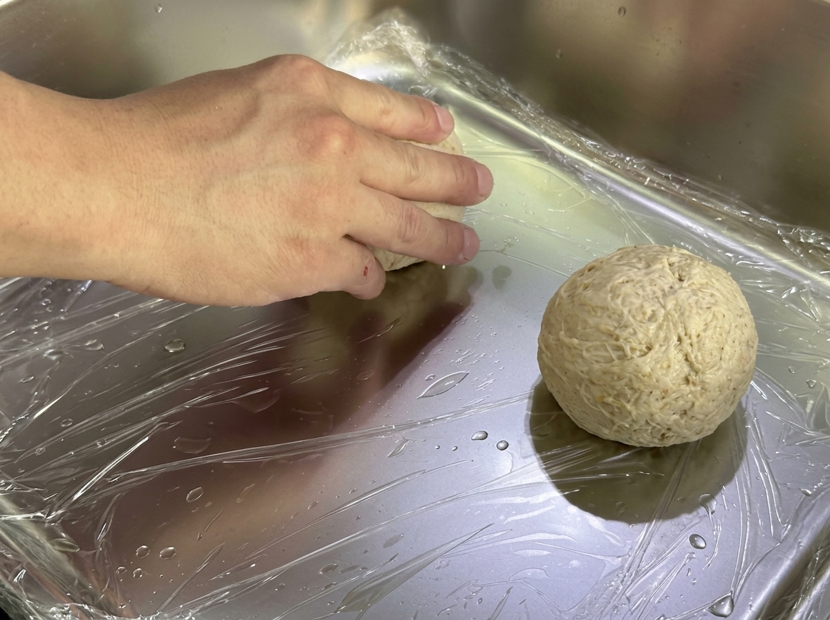 Boules de pâte disposées sur un plateau métallique recouvert de film étirable.