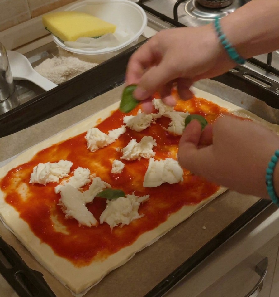 Des mains disposant des feuilles de basilic frais sur une pizza crue garnie de sauce et de fromage.