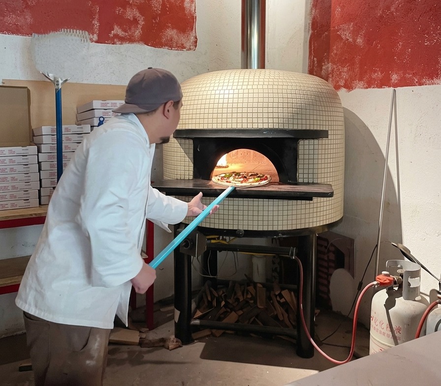 Un chef utilise une longue pelle à pizza bleue pour glisser une pizza crue dans louverture dun four à bois très chaud.