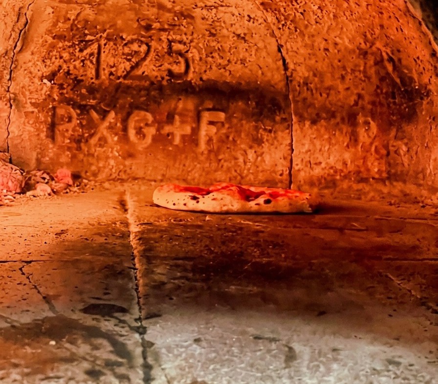 Pizza napolitaine cuisant dans un four à bois ardent, avec la croûte qui commence à gonfler.