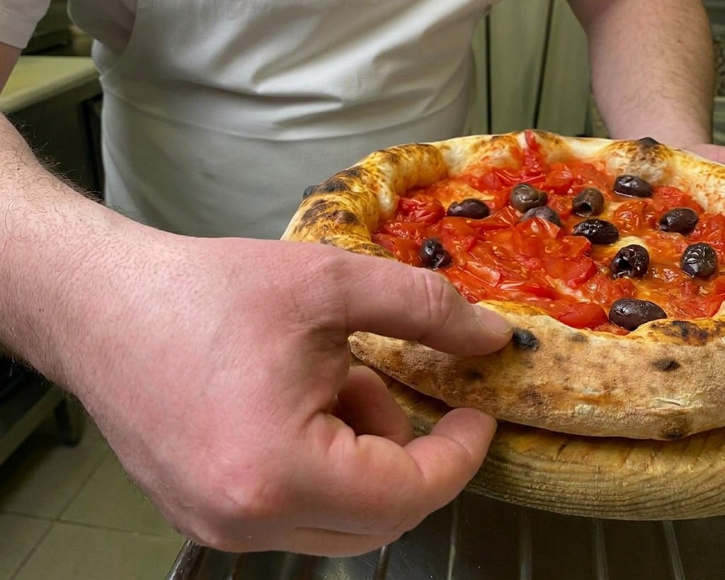 Un chef pressant du doigt la bordure épaisse et grillée dune pizza chaude aux tomates et olives pour tester sa texture élastique.