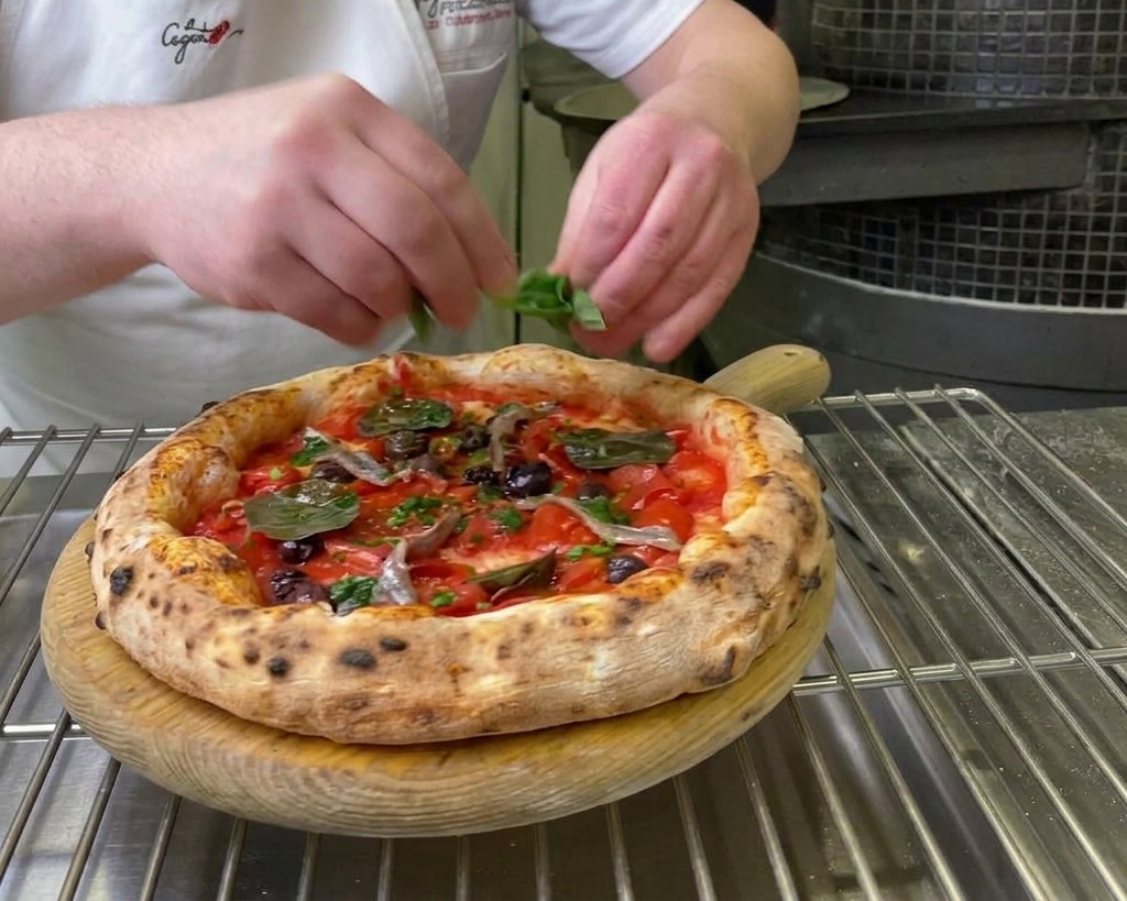Mains dun chef déposant des feuilles de basilic vert frais sur une pizza Marinara sortant du four.