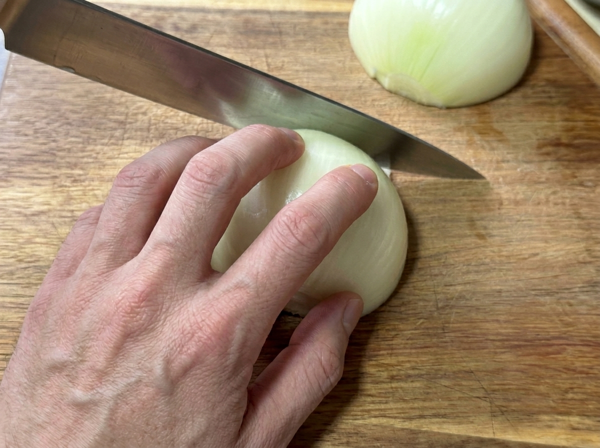 Une main coupant un oignon blanc en fines lamelles sur une planche en bois.