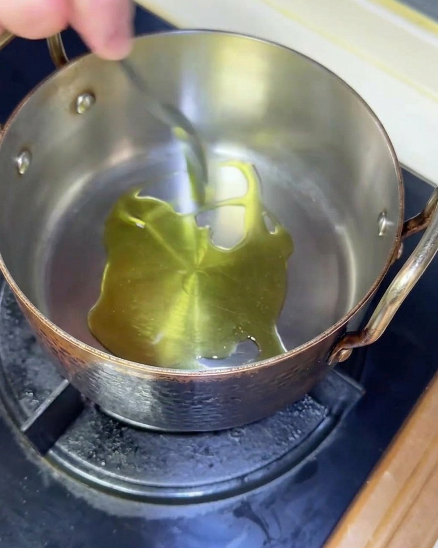 De lhuile dolive frémissante dans une sauteuse en cuivre sur une gazinière.