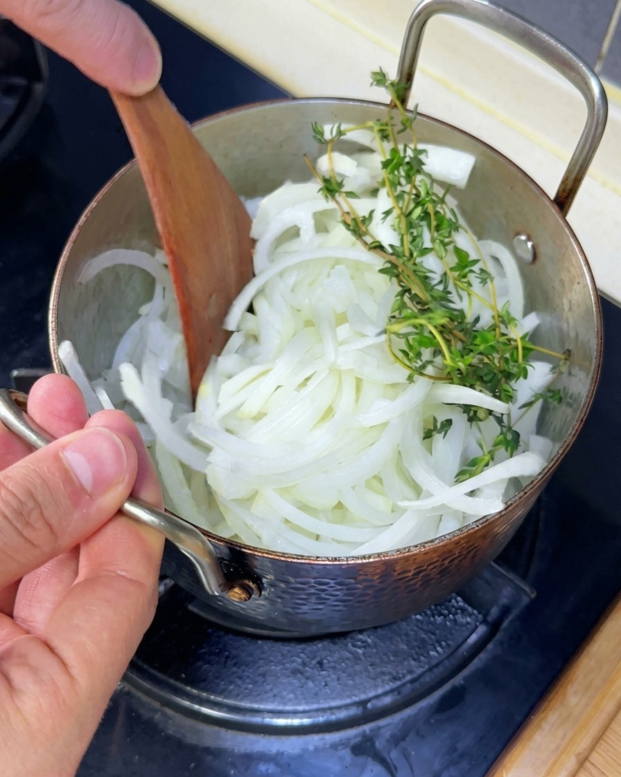 Oignons et brins de thym frais remués avec une spatule en bois dans une sauteuse.