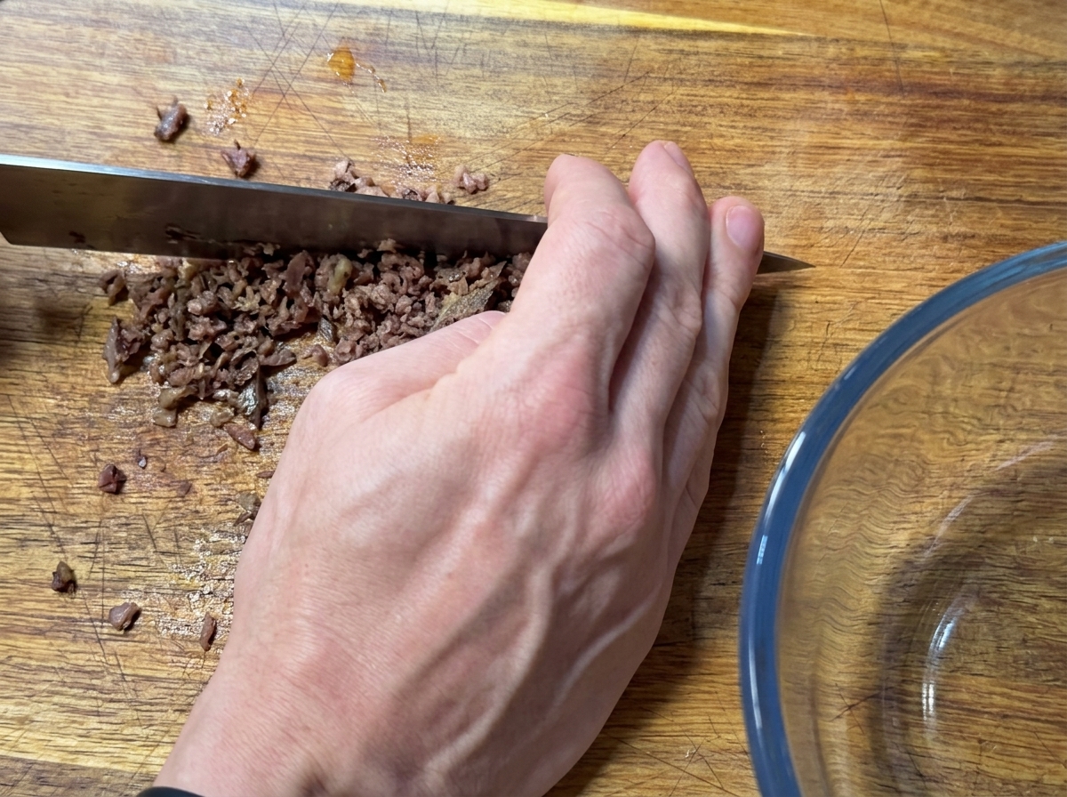 Une main utilisant un grand couteau pour hacher finement des filets danchois.