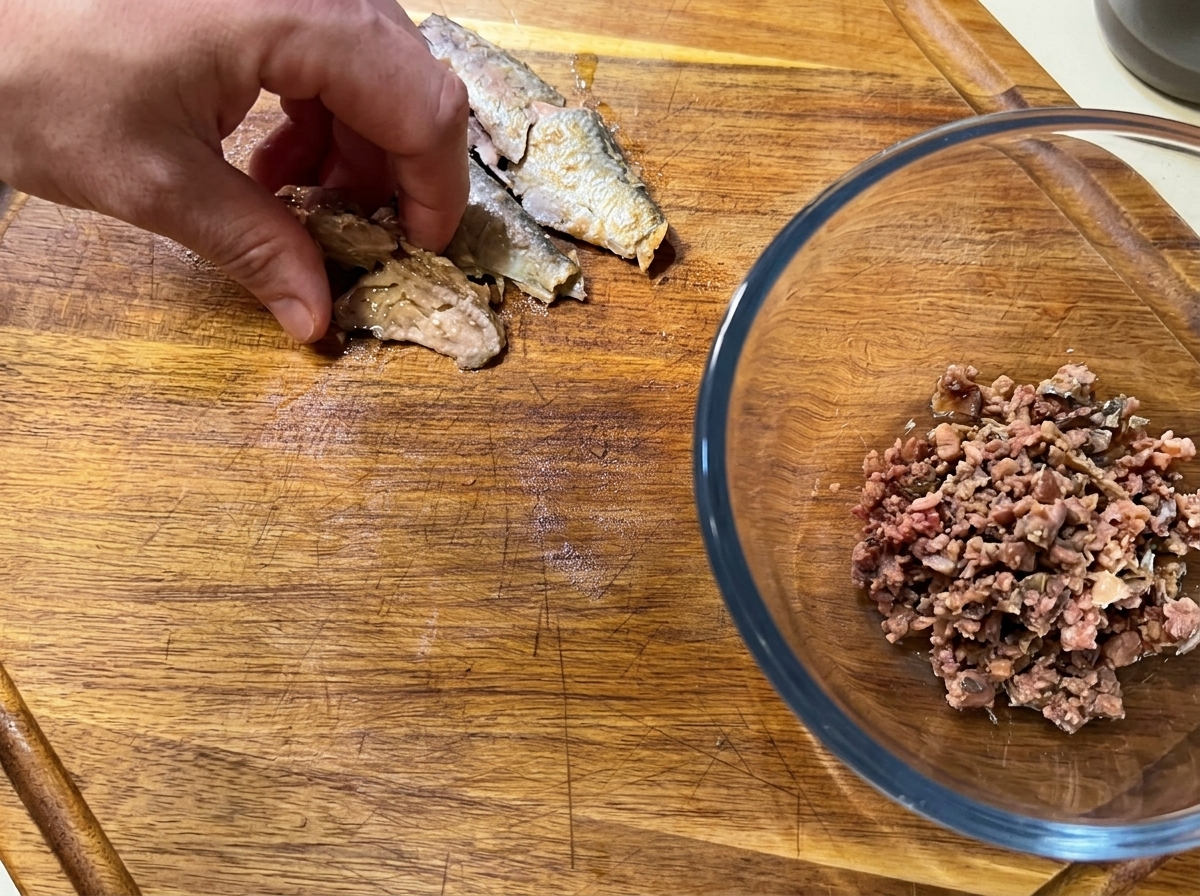 Une main désarêtant des sardines en conserve sur une planche à découper.