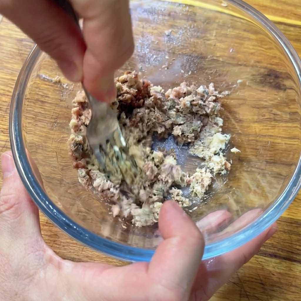 Mains utilisant une fourchette pour écraser anchois et sardines en une pâte homogène dans un bol.