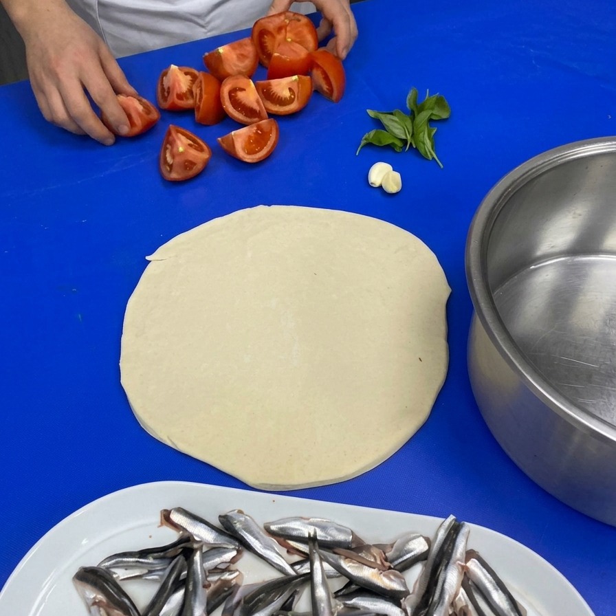 Mains du chef ramassant des quartiers de tomates, de lail et du basilic sur un plan de travail.