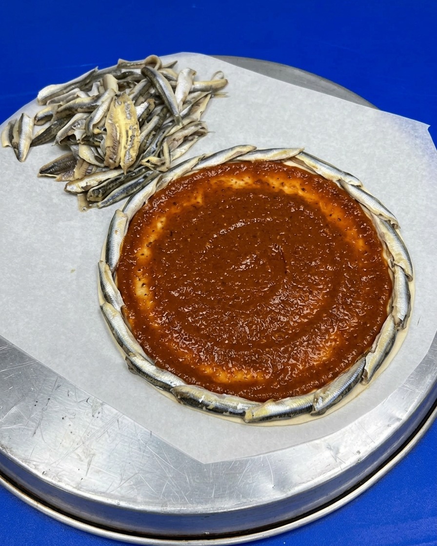 Base de pizza avec bordure danchois, nappée de sauce tomate rouge au centre.