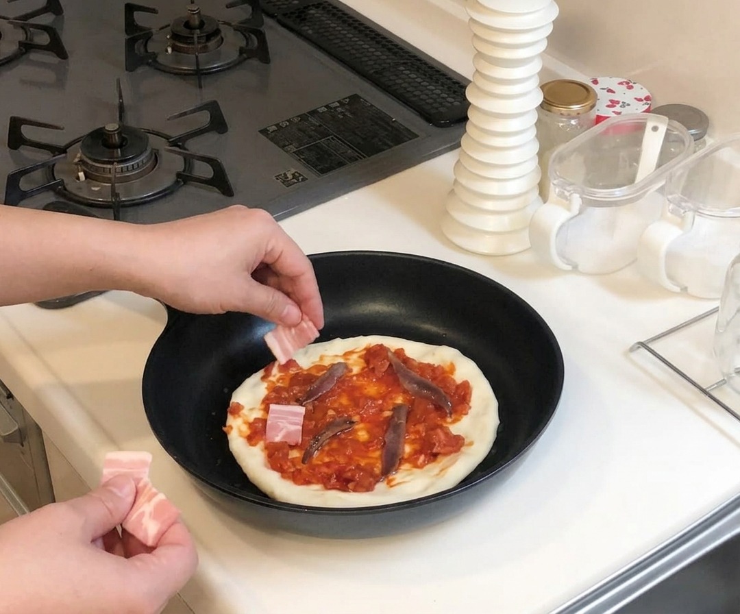 Des mains plaçant de petits morceaux de bacon cru sur une pizza garnie de sauce rouge et danchois dans une poêle.