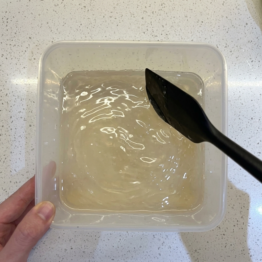 Une spatule noire mélangeant de la farine, de leau et de la levure dans un récipient transparent.