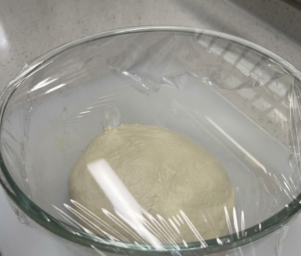 Une boule de pâte lisse reposant au fond dun bol en verre scellé avec du film plastique.