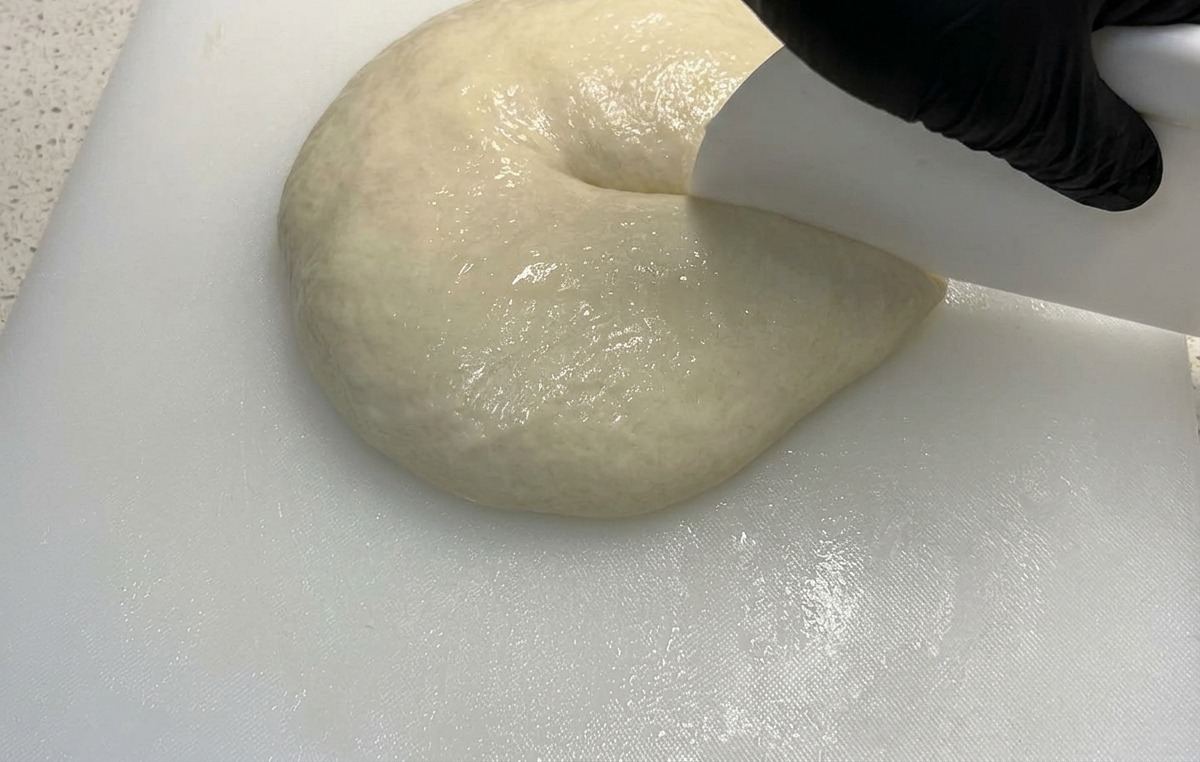 Un coupe-pâte blanc senfonçant dans une masse de pâte souple pour la diviser en deux.