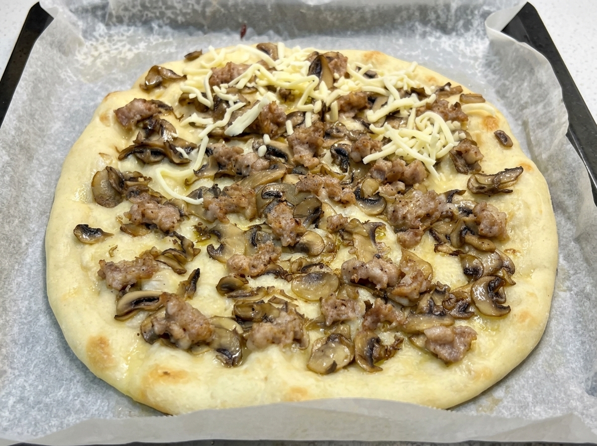 Base de pizza précuite garnie de champignons, de saucisse et parsemée de mozzarella râpée.