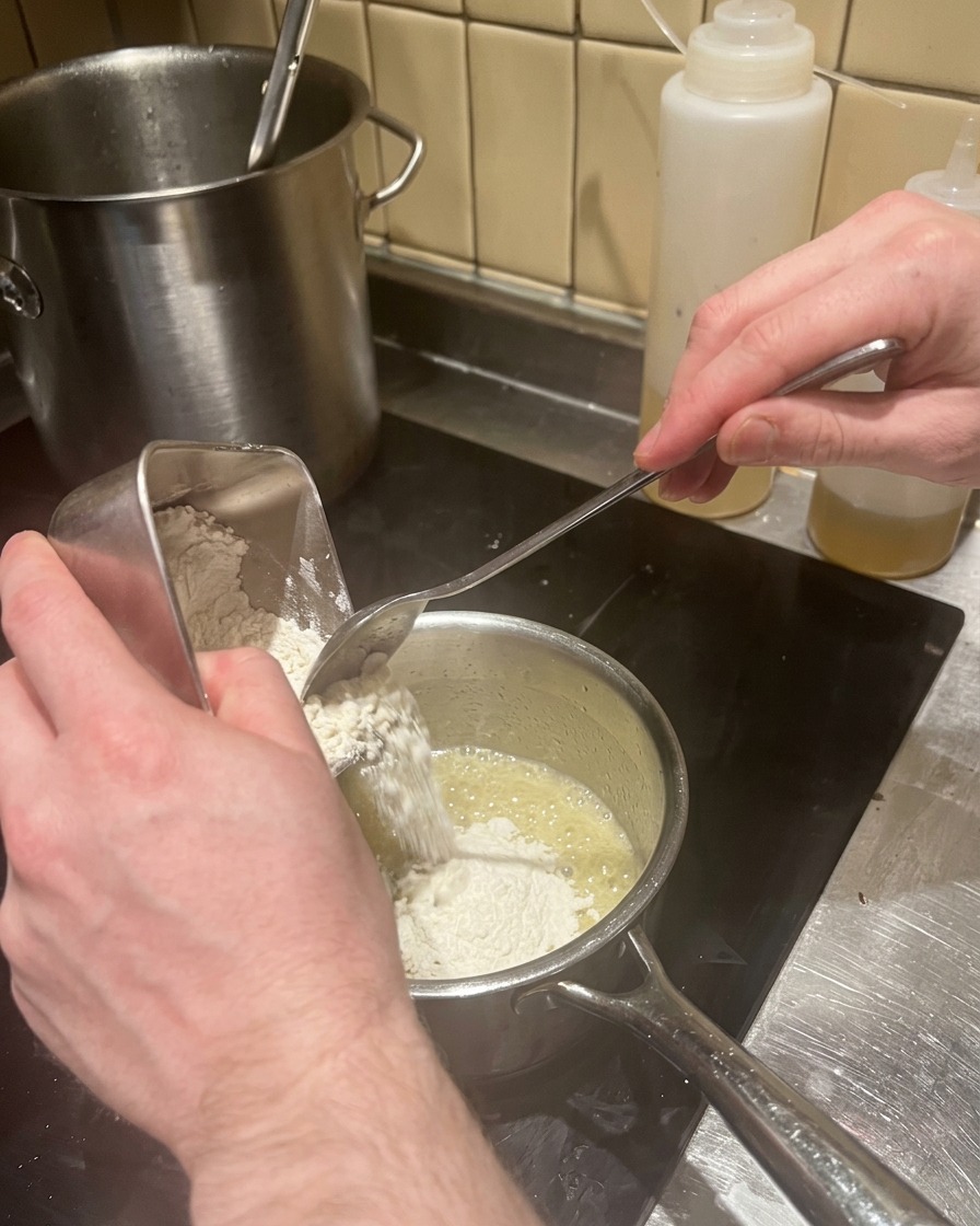 Ajout de farine dans le beurre fondu pour réaliser un roux dans une casserole.