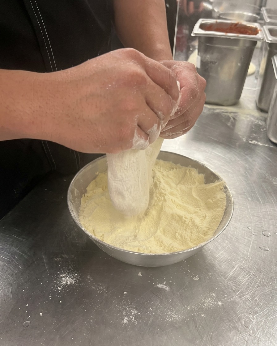 Mains pressant et étirant un pâton de pâte à pizza dans un récipient fariné.