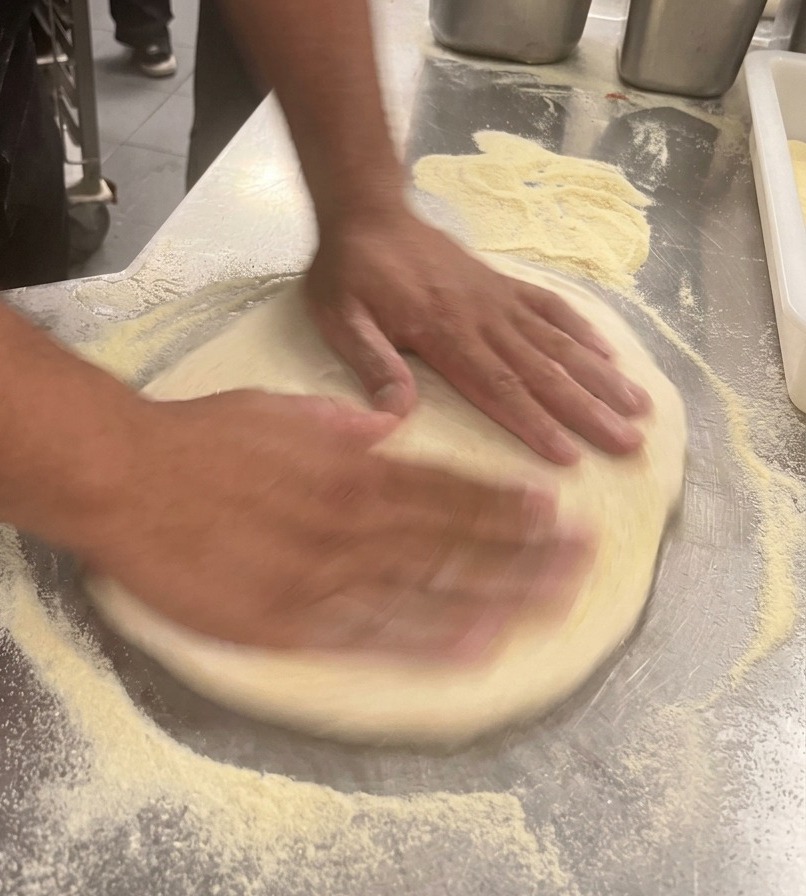 Mains dun chef étirant la pâte à pizza en un cercle plat sur un plan de travail en inox.