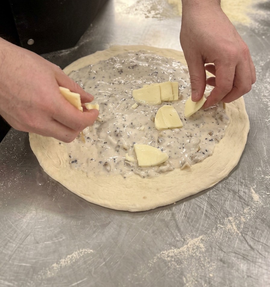 Mains répartissant des morceaux de mozzarella sur la sauce blanche de la pizza crue.