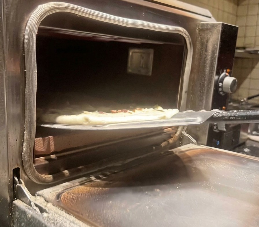 Enfournement de la pizza crue dans un four à pizza professionnel très chaud à laide dune pelle métallique.