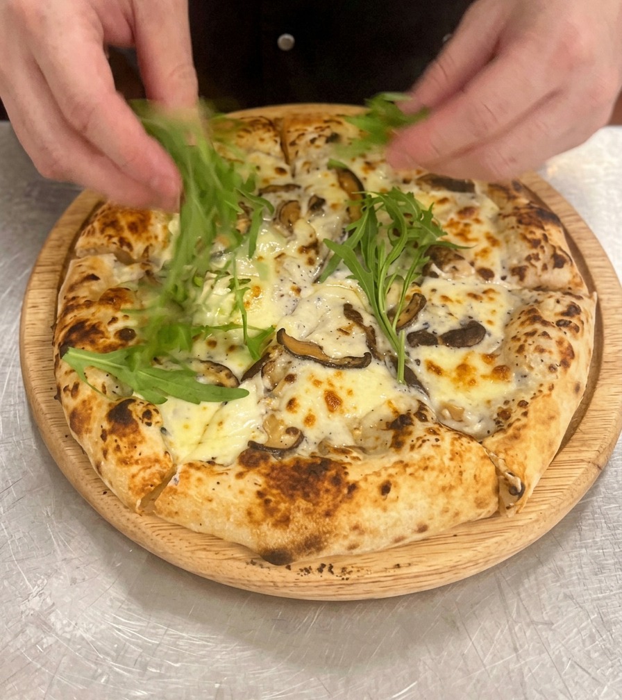 Mains disposant des feuilles de roquette dun vert vif sur la pizza coupée.