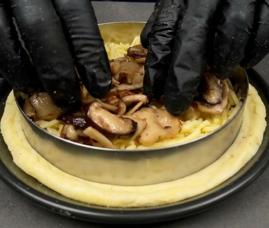 Mains déposant des champignons sautés sur un lit de mozzarella sur une base de pizza.