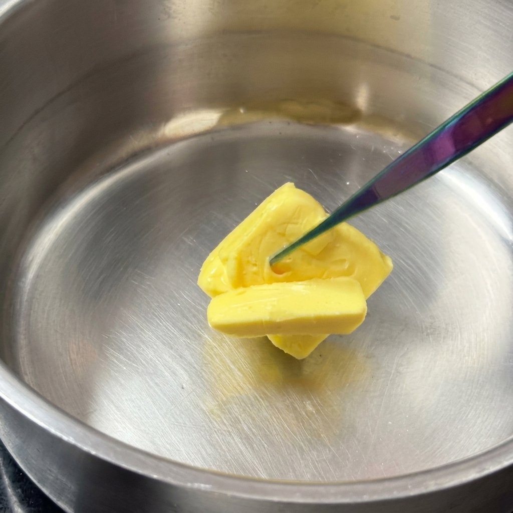 Un carré de beurre jaune fondant dans une casserole brillante en acier inoxydable.