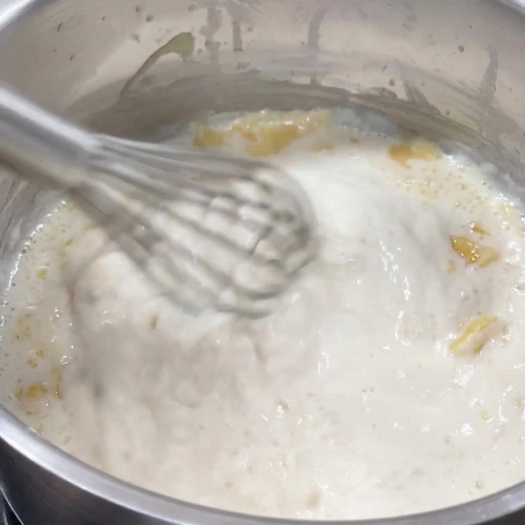 Un fouet remuant énergiquement une sauce blanche épaisse et bouillonnante dans une casserole en inox.