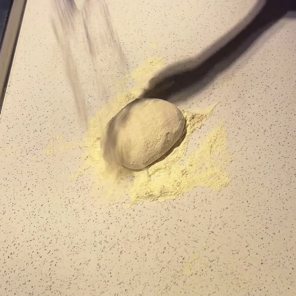 Une boule de pâte à pizza saupoudrée de farine sur un plan de travail clair.