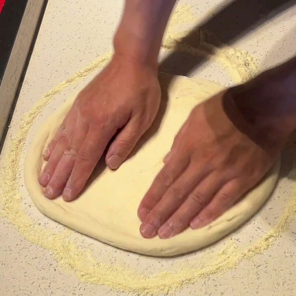 Mains pressant et étirant la pâte à pizza sur une surface farinée.