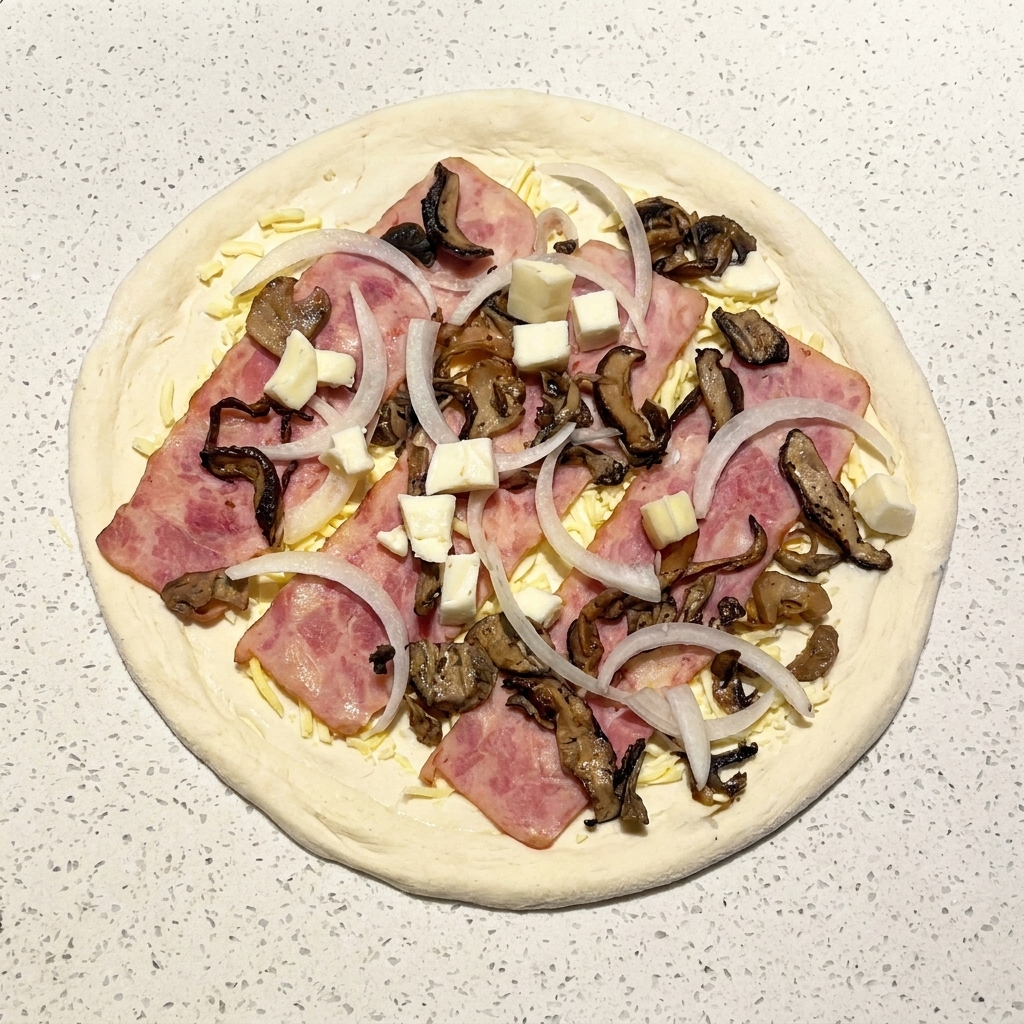 Une pizza crue garnie de bacon, champignons, oignons et petits dés de mozzarella fraîche.