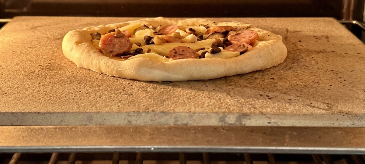 Une pizza garnie de saucisse et de champignons sur une pierre de cuisson dans un four chaud.
