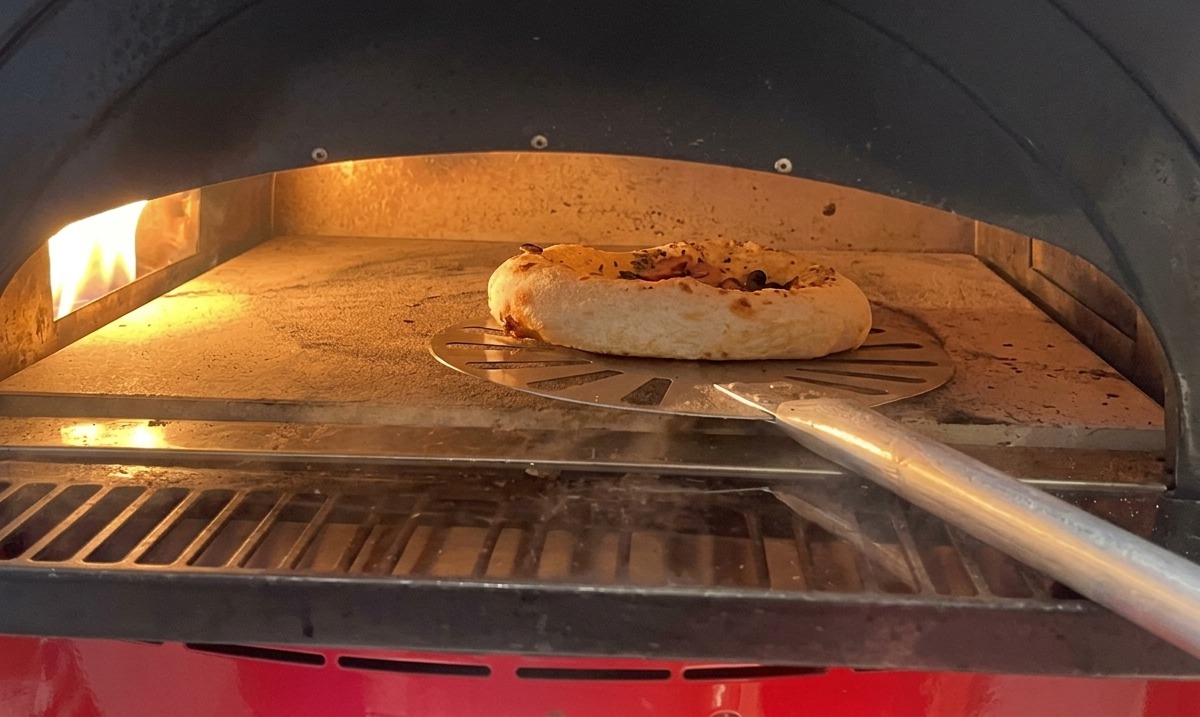 Petite pizza aux champignons et saucisse cuisant dans un four chaud, la croûte gonflant visiblement.