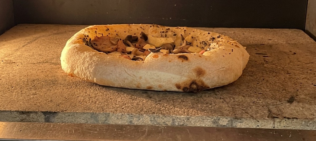 Pizza en cours de cuisson avec une croûte bien gonflée et légèrement colorée.
