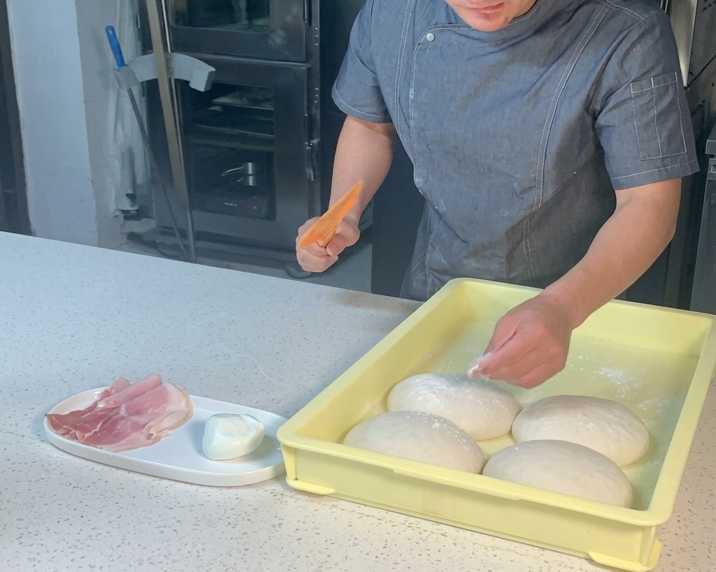 Un chef utilise une corne en plastique orange pour décoller une boule de pâte à pizza dun bac de pousse jaune.