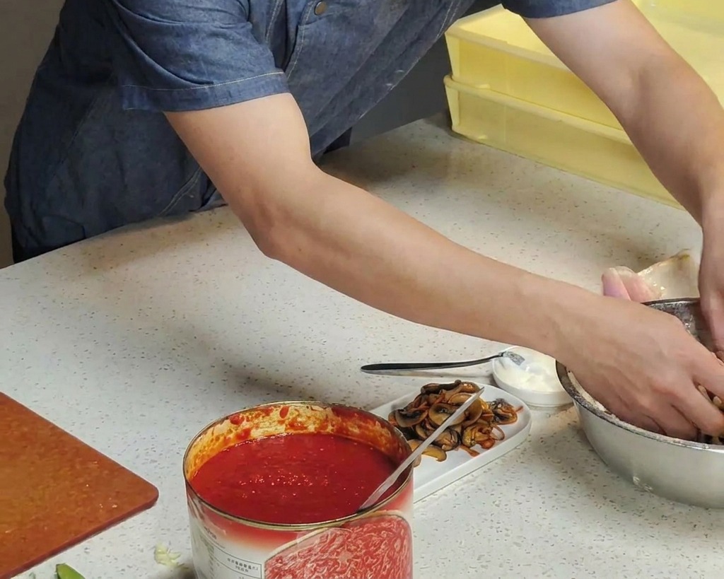Mains dun chef trempant une boule de pâte à pizza fermentée dans un bol en inox rempli de farine blanche.