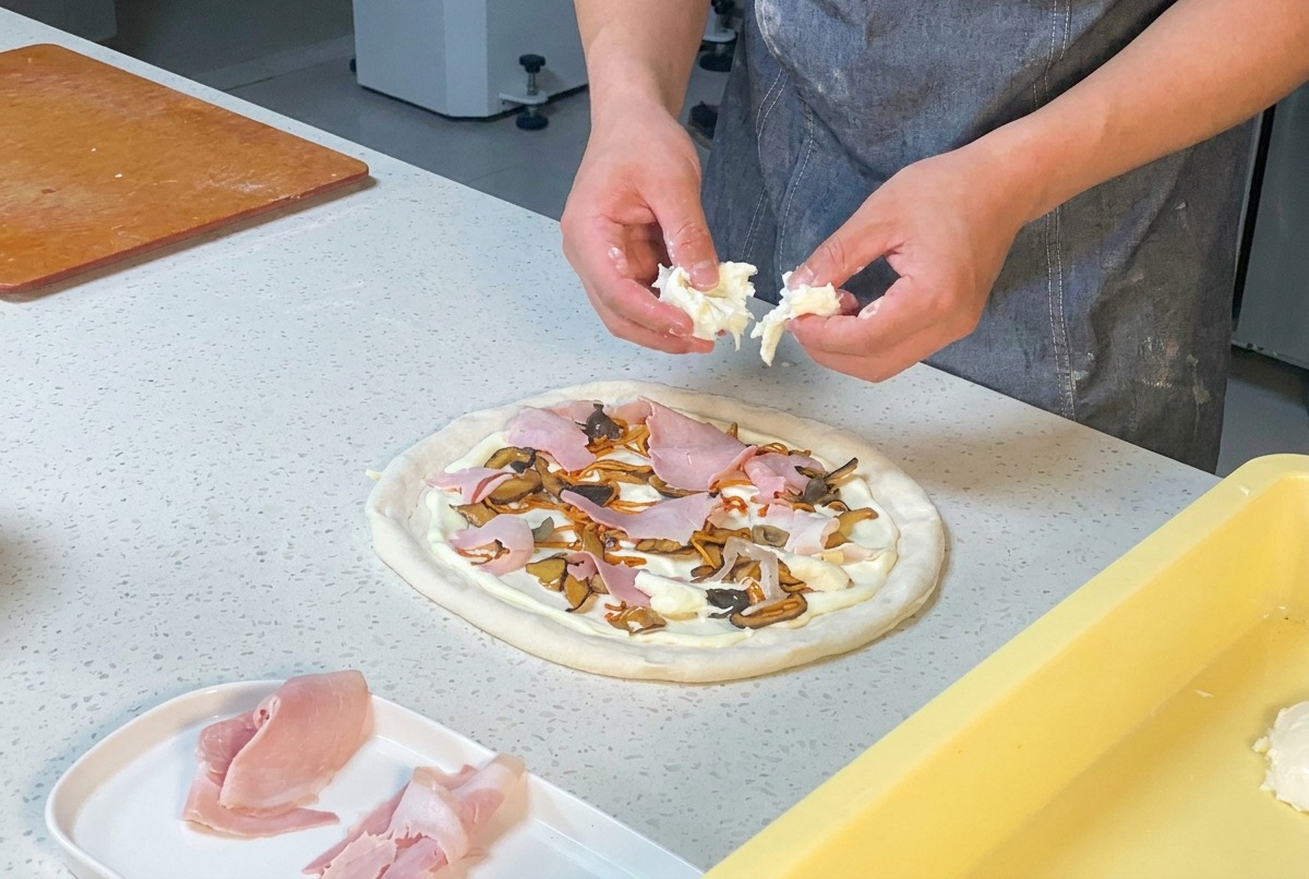 Mains dun chef déchirant de la mozzarella fraîche au-dessus dune pizza garnie de jambon, de champignons et de cordyceps.