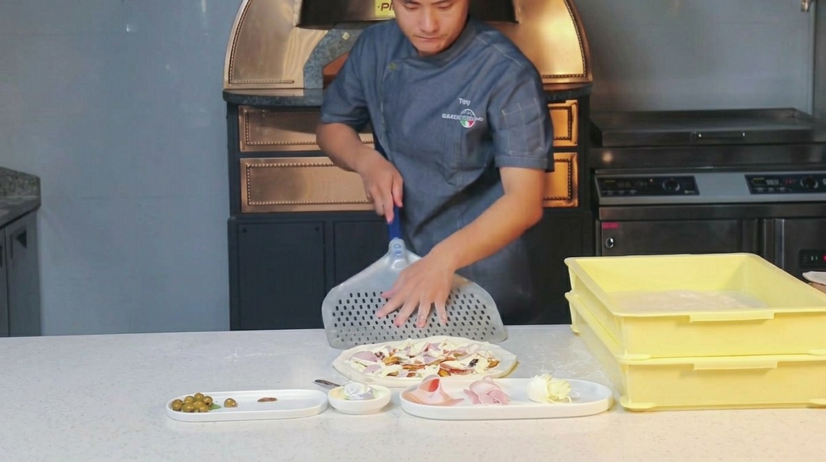 Un chef frotte de la farine sur une pelle à pizza en métal perforée.