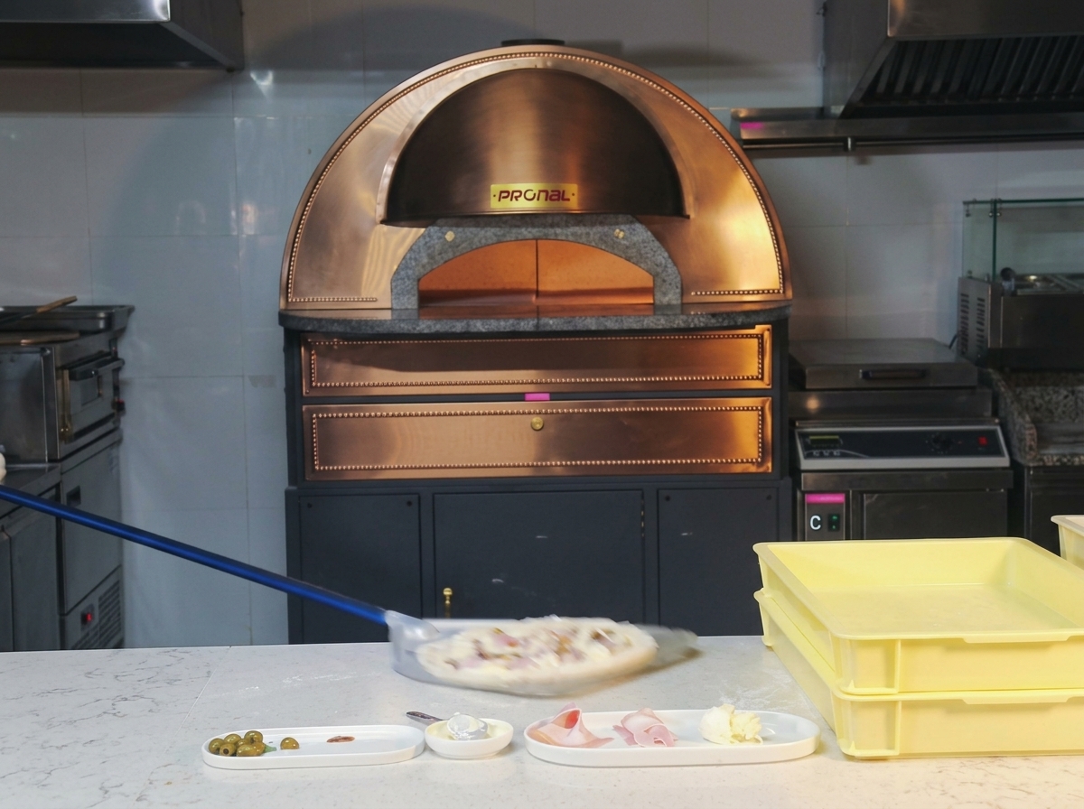 Une pizza crue au jambon et champignons glissant dune pelle à long manche vers un four à dôme incandescent.