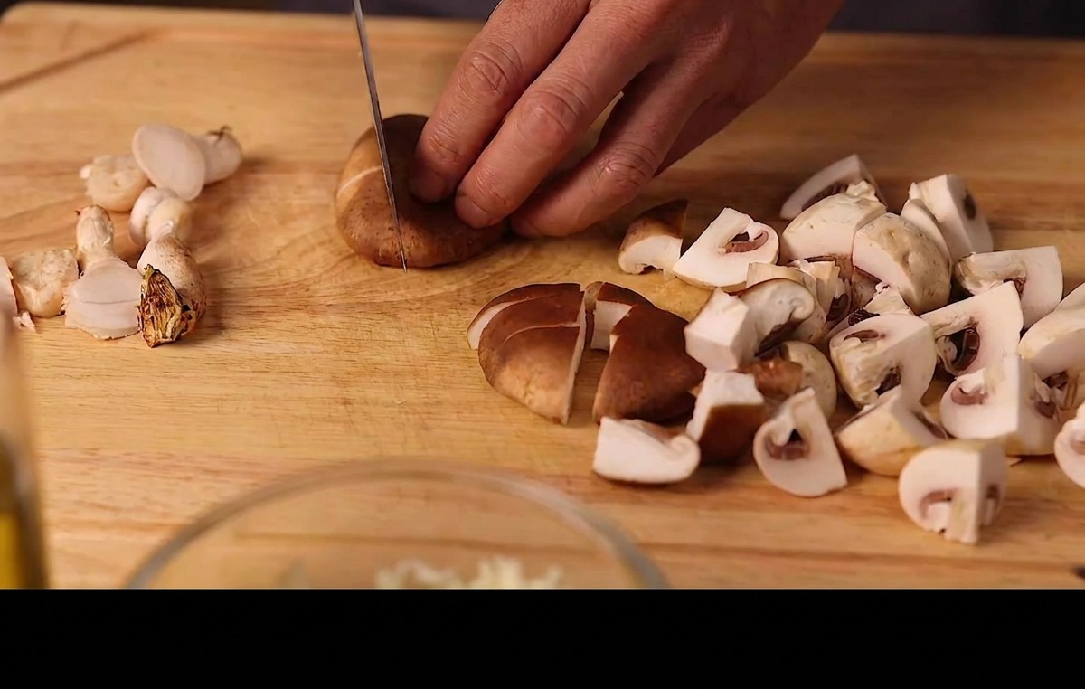 Mains coupant des shiitakés et des champignons de Paris frais sur une planche en bois.