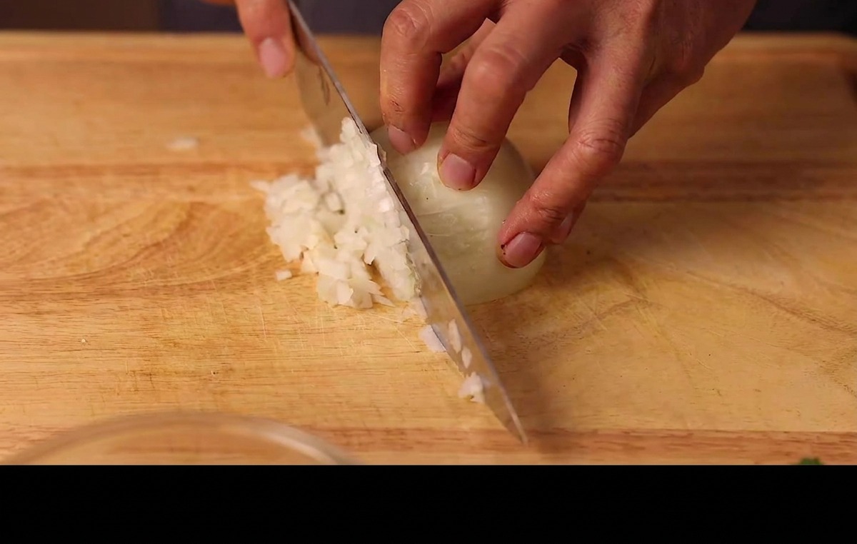 Mains hachant finement un demi-oignon blanc sur une planche à découper.